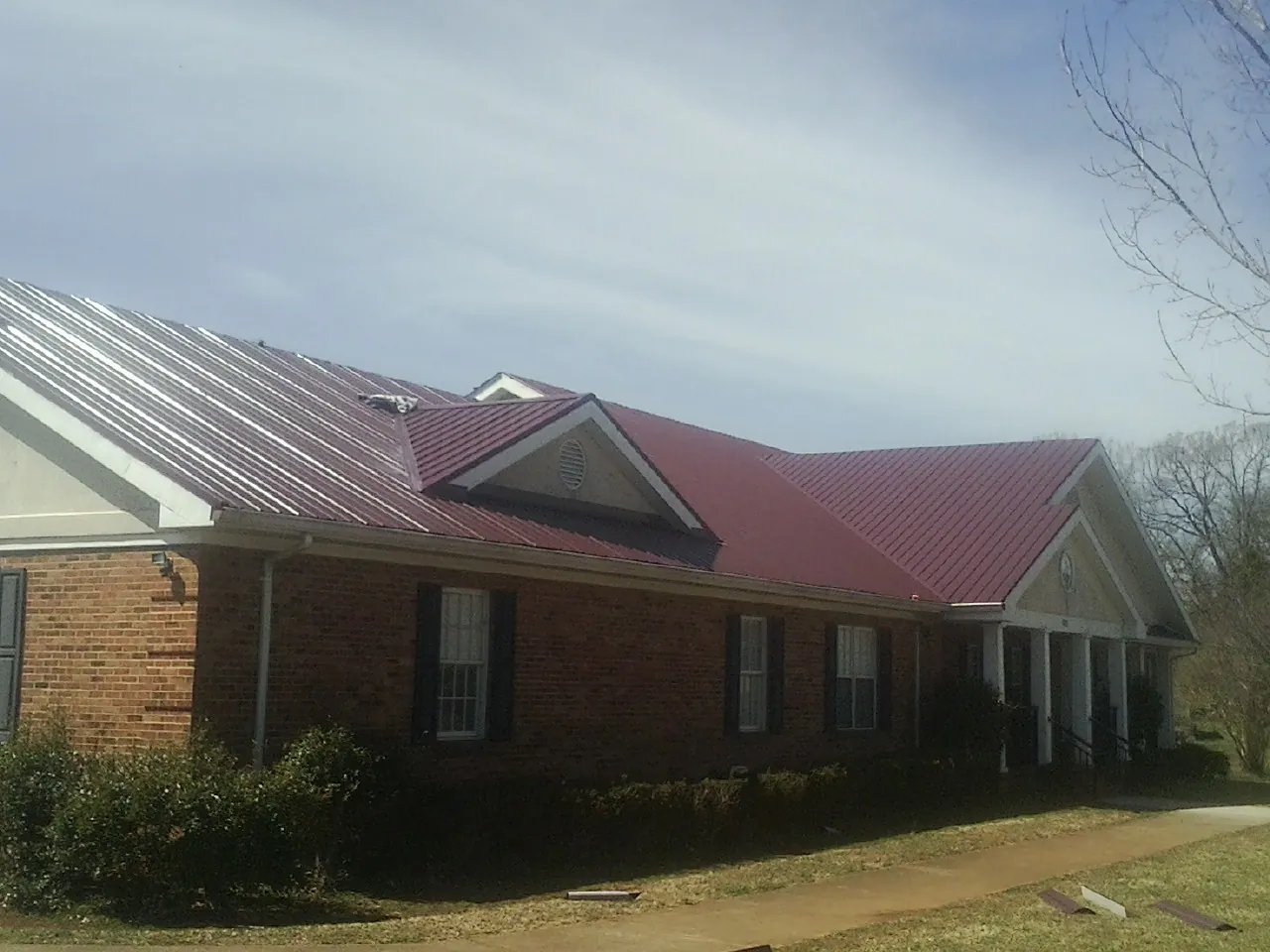 Red metal roof with gabled entries on a long brick building, from a Hail Damage Roof Repair job in Imnaha