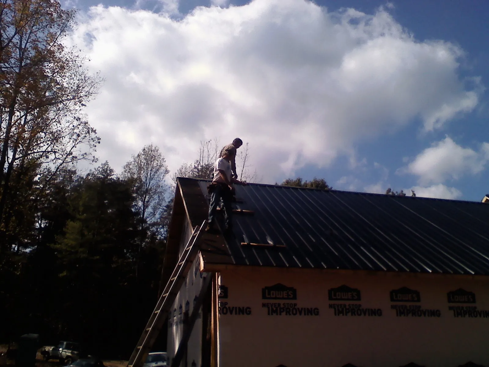 Roofer fastening dark metal panels high against a cloudy sky, from a Roof Inspection job in Imnaha