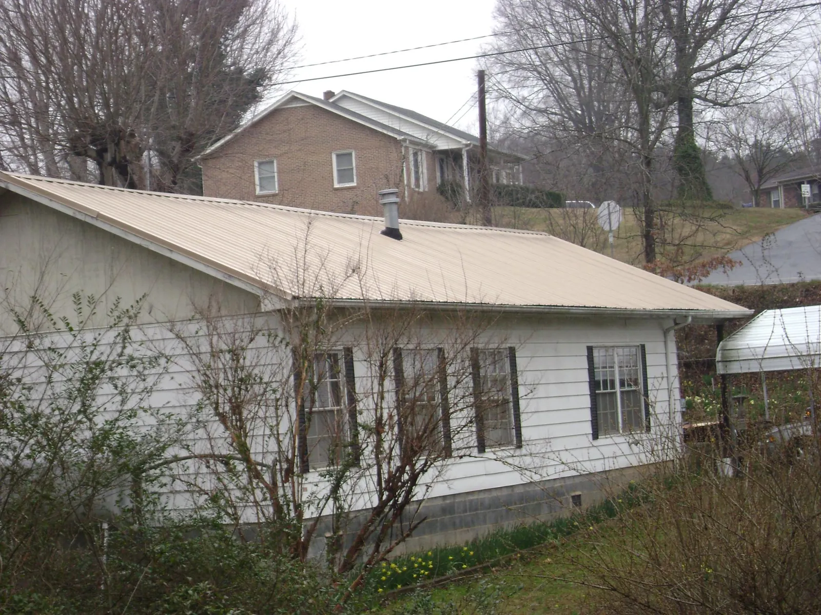 Tan metal roof on a white sided house set into a hillside — Commercial Roofing by Roofing Brothers in Imnaha